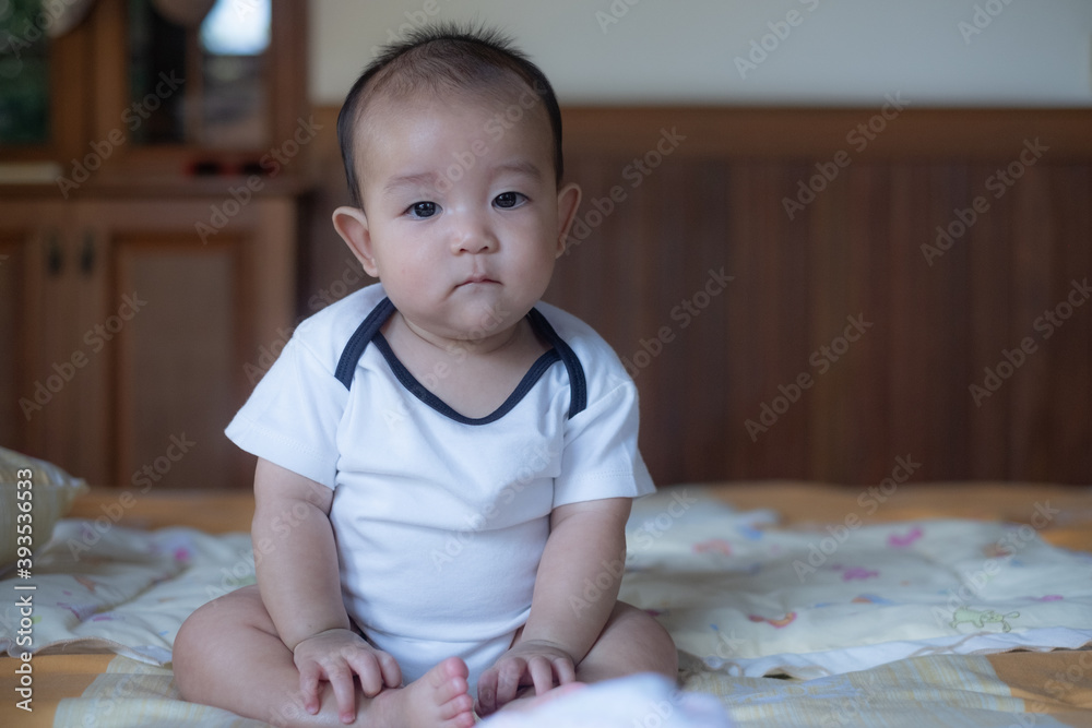 Portrait of a little adorable infant baby boy sitting on the bed and looking to camera Portrait of a little adorable infant baby boy sitting on the bed and looking to camera
