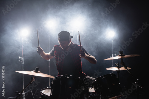 Foto Rock band member playing drums while sitting at drum kit with backlit and smoke