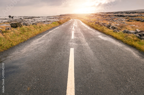 Small narrow asphalt road to a mountain. Burren region, county Clare, Ireland. Low cloudy sky. Nobody,