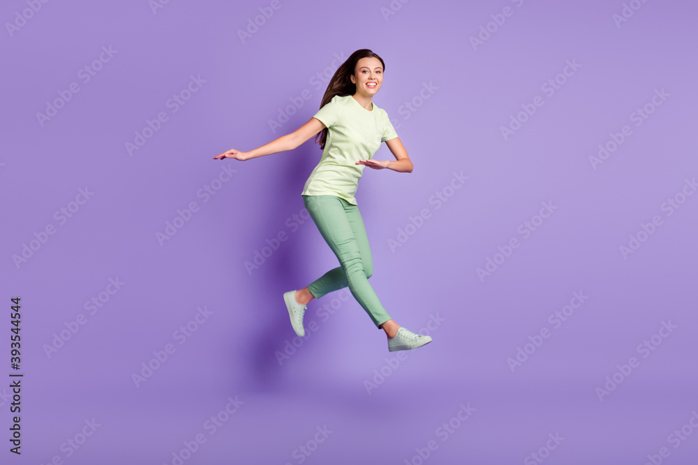 Full length portrait of attractive lady jump have fun toothy smile wear green clothing isolated on purple color background Full length portrait of attractive lady jump have fun toothy smile wear green clothing isolated on purple color background