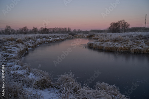Breath of winter, first ice on the lake, dawn on a frosty morning with frost on the grass, close-up of frost, patterns on the first ice. © nikolay_alekhin