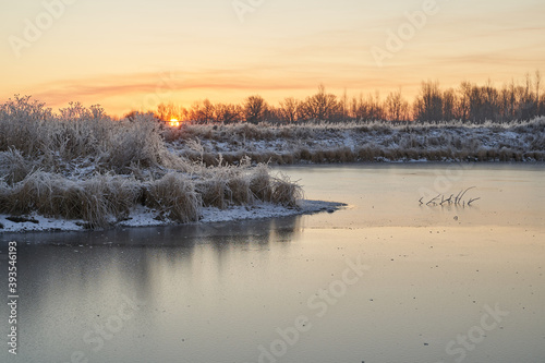 Breath of winter, first ice on the lake, dawn on a frosty morning with frost on the grass, close-up of frost, patterns on the first ice.