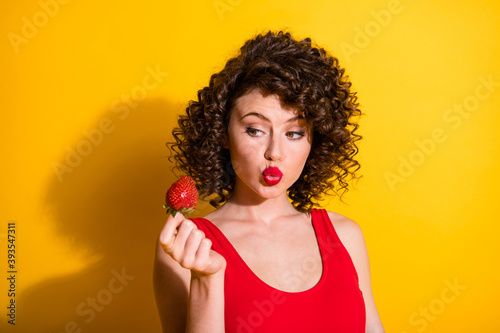 Closeup portrait photo of pretty cute young lady hold strawberry pouted lips lipstick minded imagining want eat wear red singlet unclothed shoulders isolated bright yellow color background
