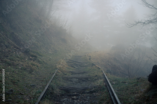 Old railway track in the Valley Val d’Astau, southwest of Bagneres de Luchon in the French Pyrenees. The trail to Lake d'Oô, Haute-Garonne, France. The rusty rails go into the misty winter forest.