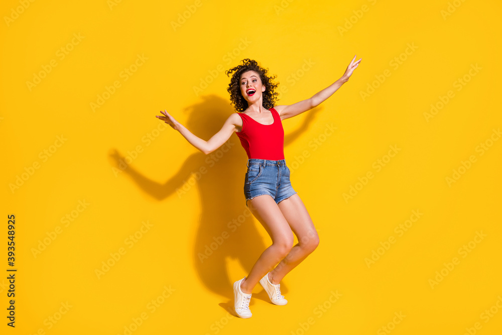 Full length body size photo of nice girl with curly hair dancing moving smiling satisfied at party singing standing tiptoes isolated on vivid yellow color background Full length body size photo of nice girl with curly hair dancing moving smiling satisfied at party singing standing tiptoes isolated on vivid yellow color background