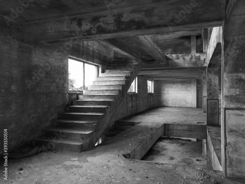 Staircase between floors in an empty messy industrial warehouse, urban exploration of the interior of an abandoned building, with broken windows and large pillars, concrete structure © slobodan