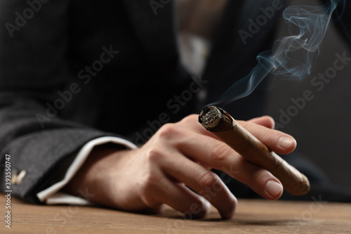 Close-up of man s hand resting on table  holding a lit cigar