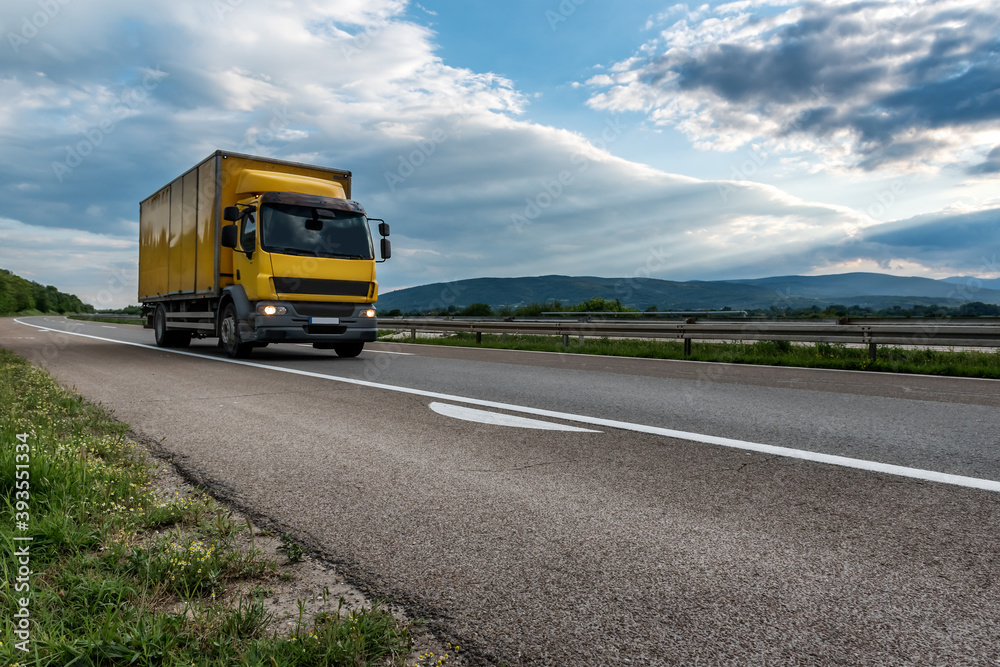 Highway transportation traffic scene with Yellow Cargo Delivery Truck speeding down the road
