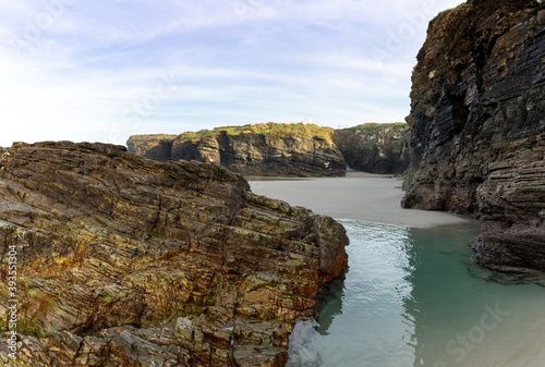 sandy beach with tidal pools and jagged broken cliffs behind in warm evening light