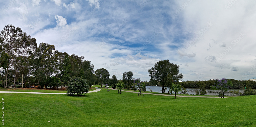 Naklejka premium Beautiful panoramic view of a park with green grass, tall trees and paved trail for walking and cycling, Reid Park, Parramatta Cycleway, Rydalmere, Sydney, New South Wales, Australia 