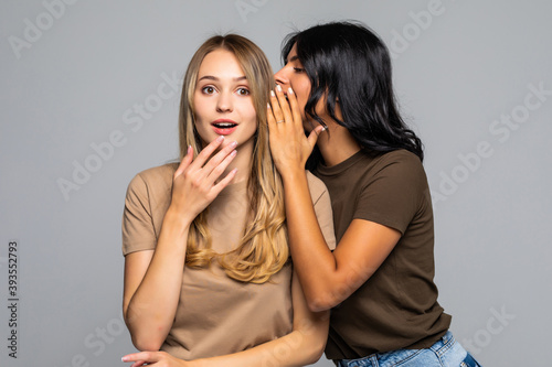Two beautiful women telling secret isolated on white background