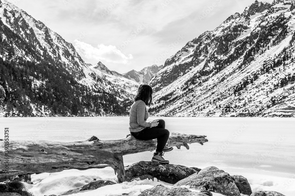 Beautiful young woman sitting next to stunning winter landscape. Concept of travel and adventure at the frozen Gaube Lake (Lac de Gaube) in the French Pyrenees, Cauterets, France. Beautiful young woman sitting next to stunning winter landscape. Concept of travel and adventure at the frozen Gaube Lake (Lac de Gaube) in the French Pyrenees, Cauterets, France.