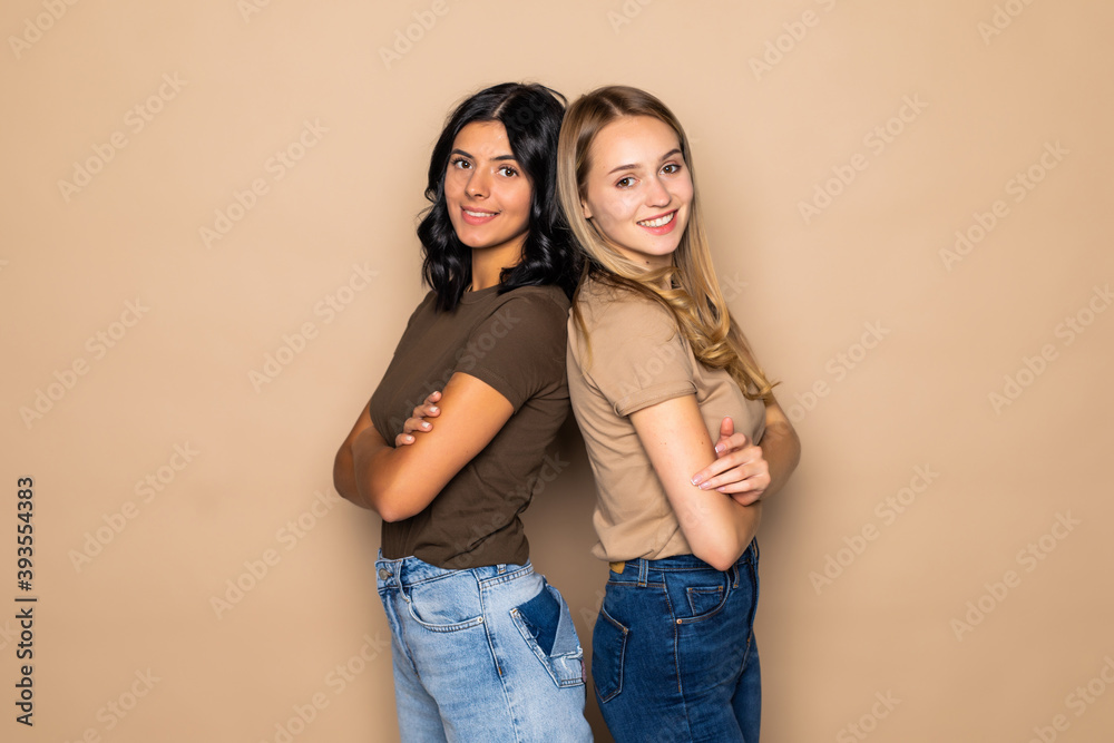 Two beautiful young women posing camera over beige background Two beautiful young women posing camera over beige background