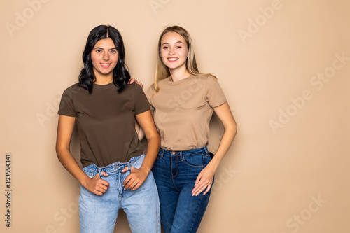 Two beautiful young women posing camera over beige background