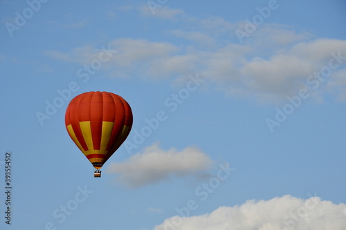 Close up on a red and yellow balloon with a big basket underneath flying through the cloudy sky full of clouds next to a dense forest or moor seen on a sunny summer day on a Polish countryside © Rafal