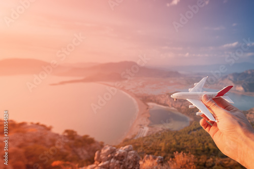 Hand holding a toy airplane on the background of the sea beach and lagoon at sunset. Concept of opening new flights in airlines and air transport photo