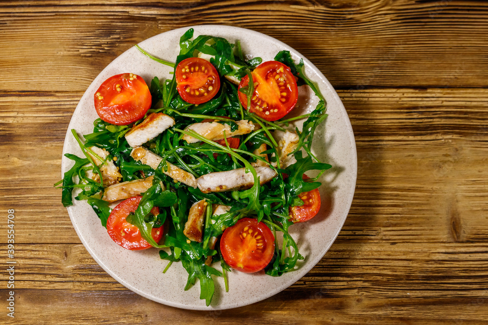 Tasty salad of fried chicken breast, fresh arugula and cherry tomatoes on wooden table. Top view