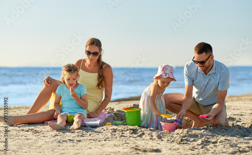 family and leisure concept - happy father, mother and two little daughters playing with sand toys on summer beach