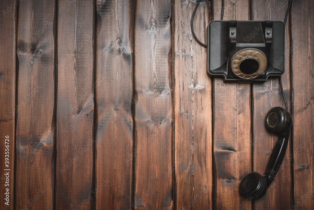 Fototapeta premium Black rotary phone on the brown wooden desk background with copy space.
