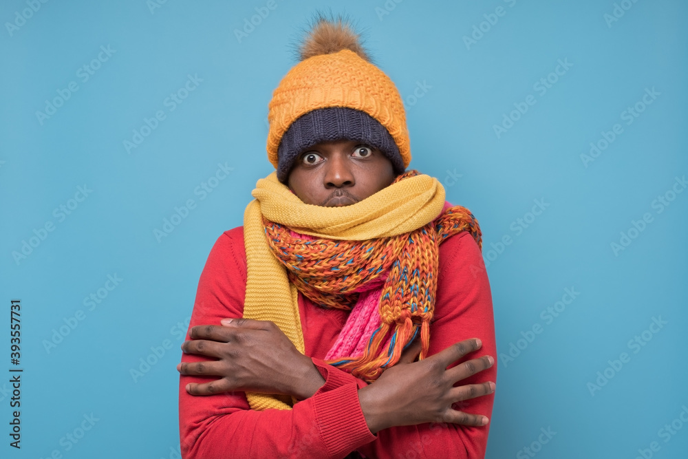 Funny african american mature man in yellow scarf and hat freezing in warm clothing. Studio shoot on blue wall. Funny african american mature man in yellow scarf and hat freezing in warm clothing. Studio shoot on blue wall.