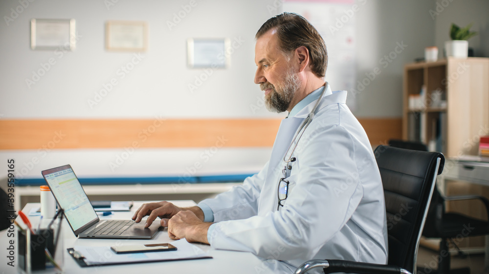 In a Doctor's Consultation Office: Experienced Physician Working on a Laptop, Prescribing Medicine, Analysing Tests Results. Health Care Specialist Planning Treatment. Side View Shot. In a Doctor's Consultation Office: Experienced Physician Working on a Laptop, Prescribing Medicine, Analysing Tests Results. Health Care Specialist Planning Treatment. Side View Shot.