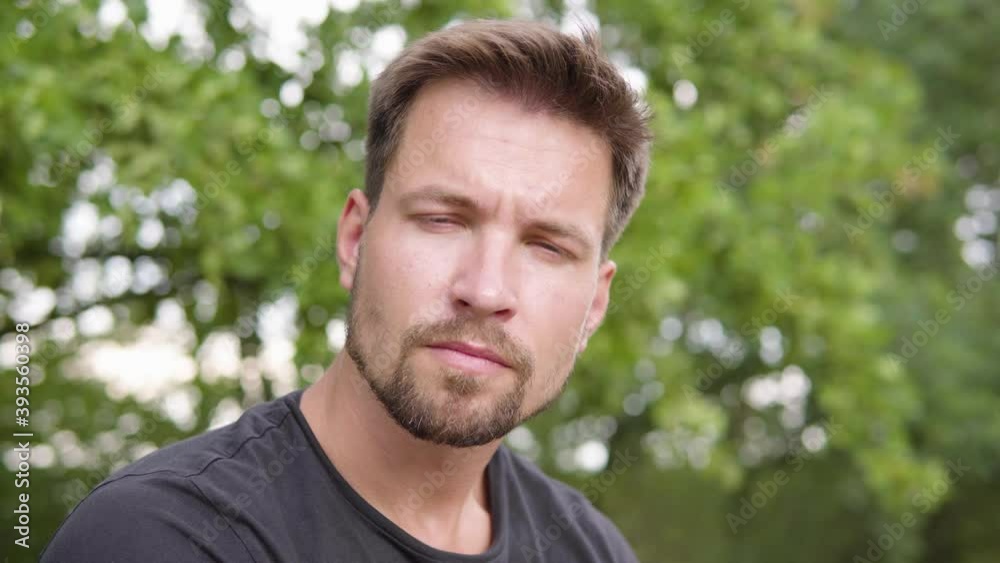 A young handsome man looks down at the camera, looking sad - face closeup - a tree in the blurry background A young handsome man looks down at the camera, looking sad - face closeup - a tree in the blurry background