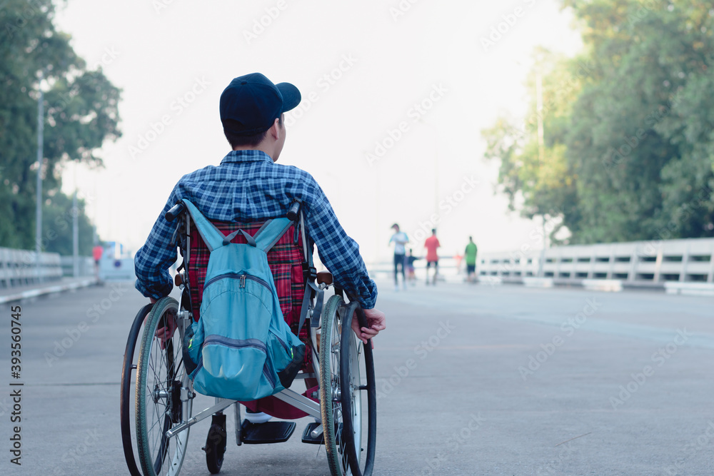 Asian special child on wheelchair wearing blue shirt and cap with backpack learn how to use wheelchairs on public street,Lifestyle in the education age of disabled children,Happy disabled kid concept.