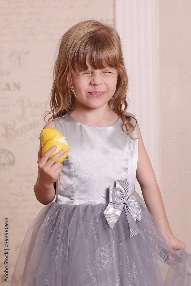 little blond baby girl eating sore lemon and grimacing on retro wall interior background little blond baby girl eating sore lemon and grimacing on retro wall interior background