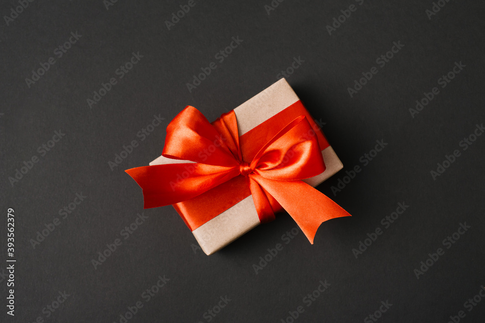 Present box with red bow on black background. Flat lay, top view, copy space.