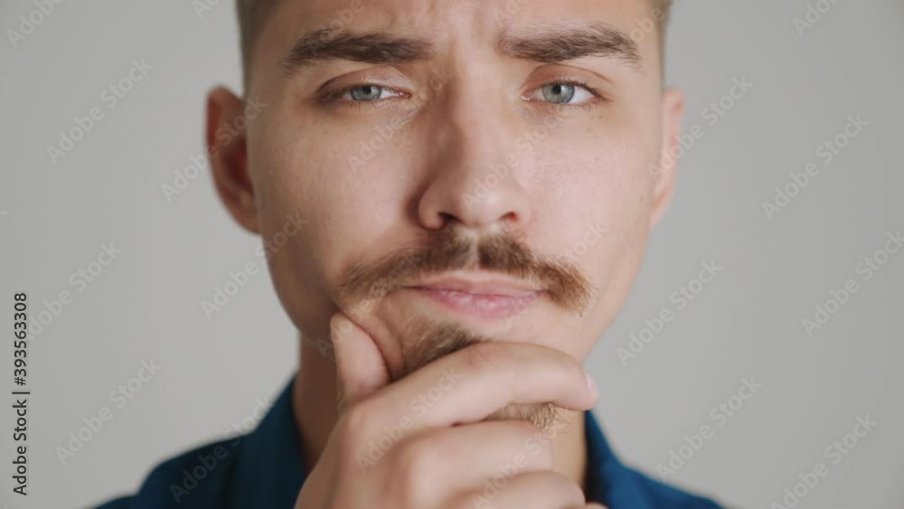 A close-up view of a handsome man is thinking about something standing isolated over gray background in studio A close-up view of a handsome man is thinking about something standing isolated over gray background in studio