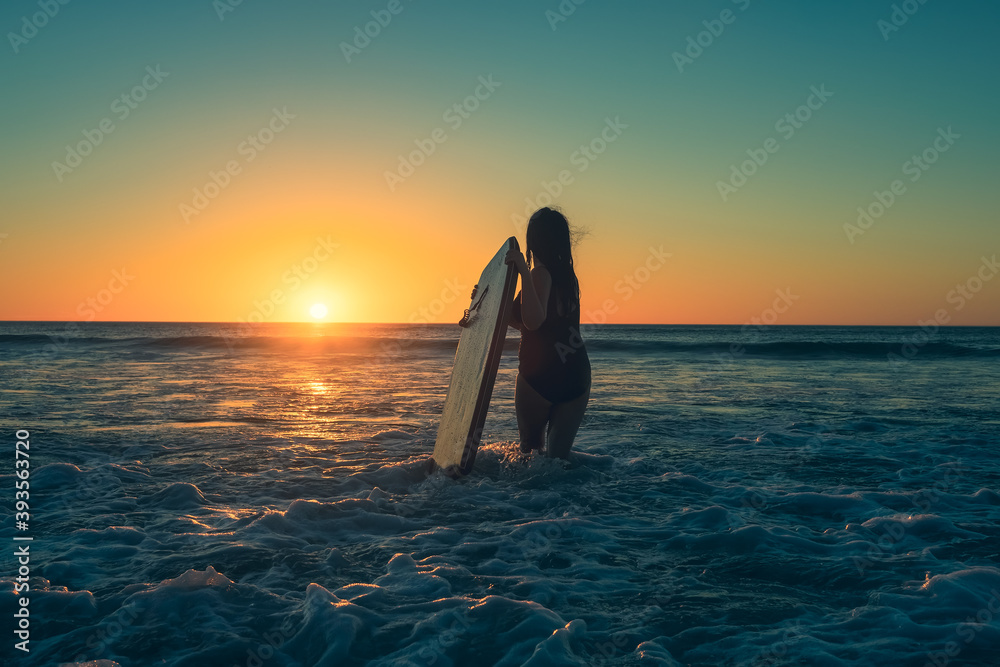 Woman with bodyboard entering the water to catch some waves at Moana Beach during sunset in South Australia