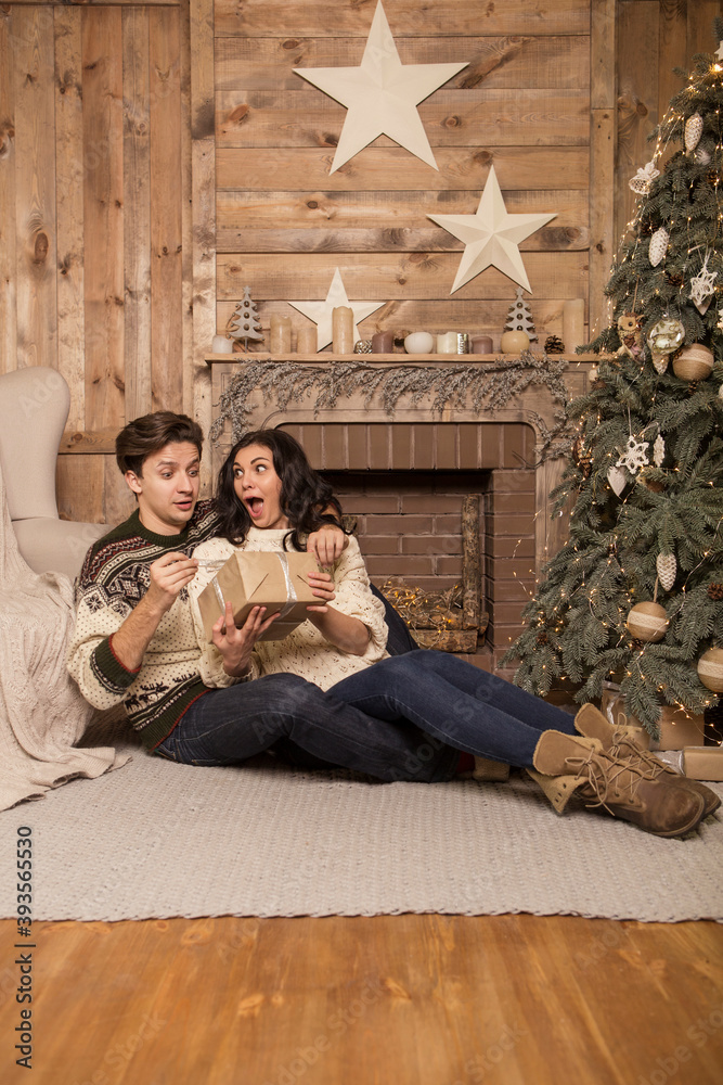 Naklejka premium Beautiful brunette caucasian romantic loving couple in cozy warm sweaters in the cabin on a christmas new year eve, smiling, kissing, having fun with each other. Dim dark night light, toned image