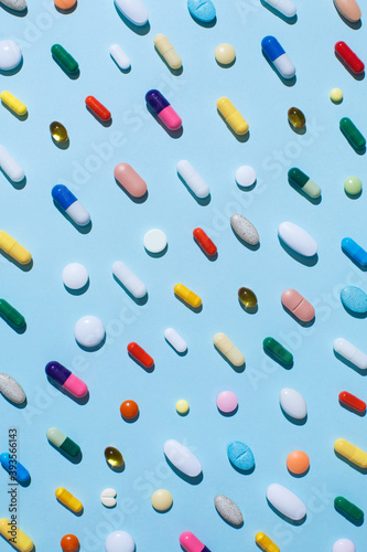 Creative layout of colorful pills and capsules on blue background with summer sun and sharp shadow. Minimal medical concept. Pharmaceutical, Covid-19 or Coronavirus. Flat lay, top view. photo