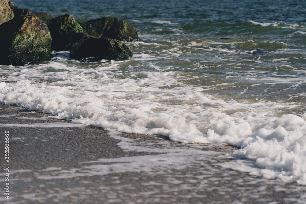 Sea wave spreading on the beach became a sea foam near the rocks Sea wave spreading on the beach became a sea foam near the rocks