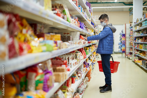 Boy teenager wearing a protective mask takes food from the shelf in a grocery store