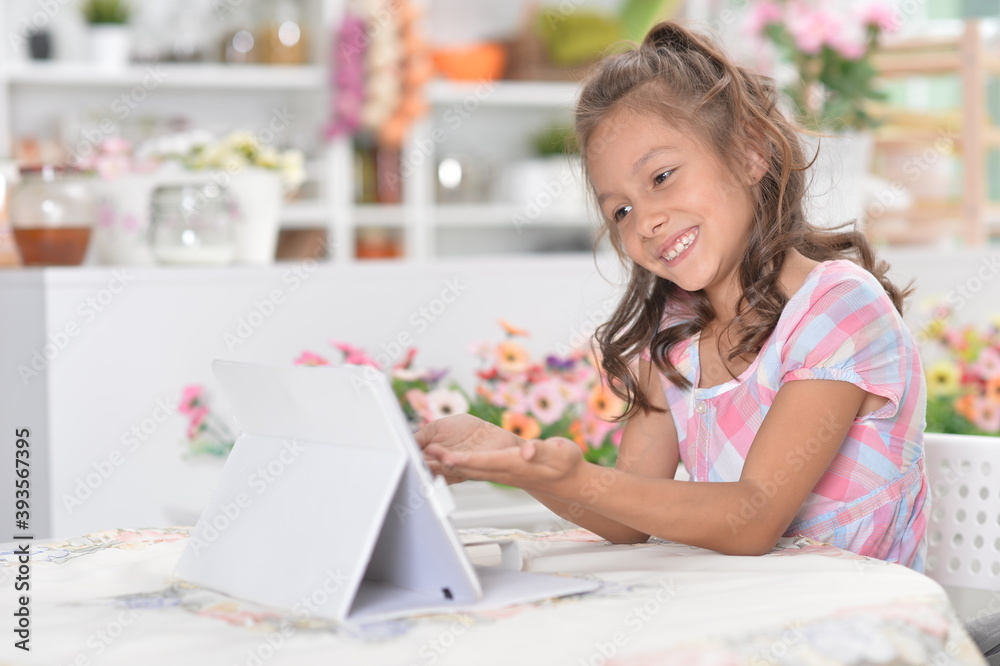 Little girl sitting at table and using modern tablet Little girl sitting at table and using modern tablet