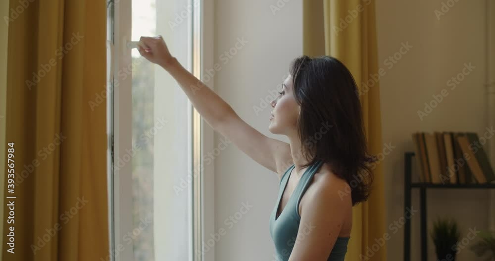 Side view of elegant woman opening window to breath fresh air slow motion. Sensual girl in sport bra standing by window looking outdoors natural light. Freshness energy sportive fashion concept Side view of elegant woman opening window to breath fresh air slow motion. Sensual girl in sport bra standing by window looking outdoors natural light. Freshness energy sportive fashion concept