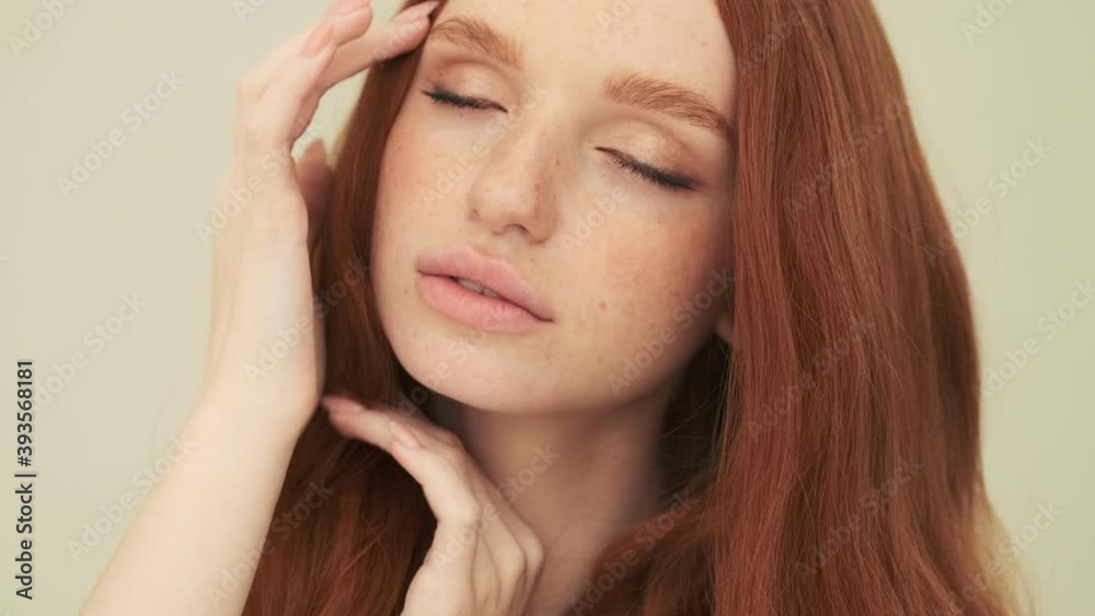 A charming woman is posing to the camera while touching her hair standing isolated over beige background in studio A charming woman is posing to the camera while touching her hair standing isolated over beige background in studio