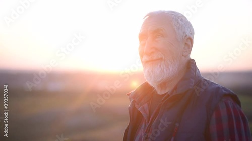 Senior man with gray hair and beard in the plaid shirt on the background of the mountain at sunset