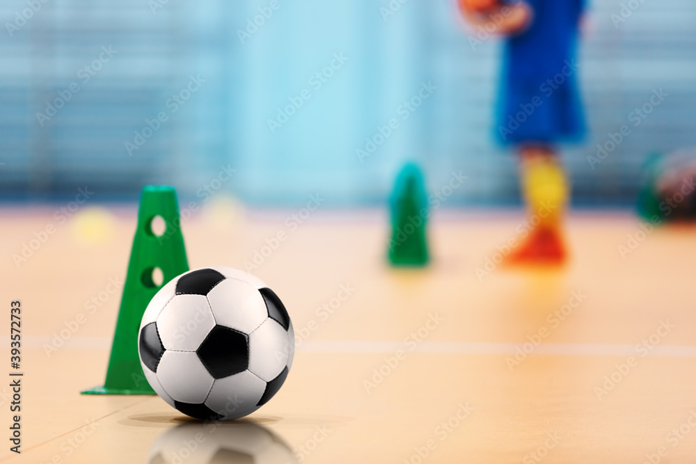 Fototapeta premium Indoor soccer - futsal training field. Soccer ball and training cones. Kids on practice in blurred background