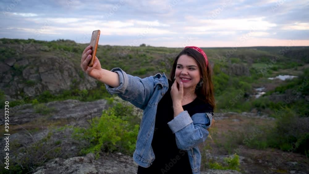 Brunette girl with a hairband and jeans jacket invites to follow her in the background of canyon