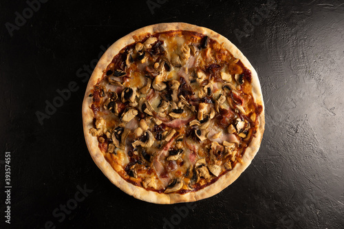 Classic round thin crust pizza with bacon, mushrooms and cheese on a dark background.