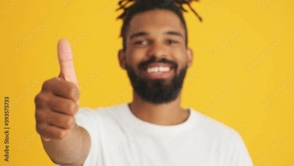 Young handsome cheerful african man showing thumbs up isolated over yellow background Young handsome cheerful african man showing thumbs up isolated over yellow background