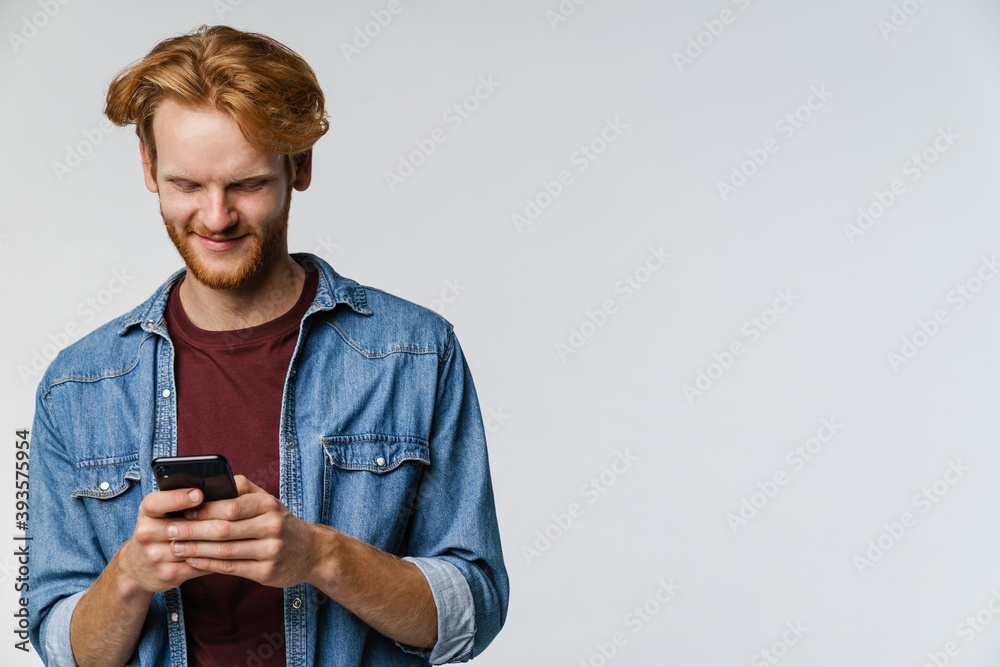 Fototapeta premium Joyful caucasian redhead guy smiling while using cellphone
