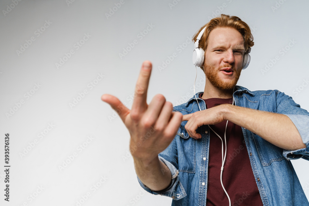 Naklejka premium Happy redhead guy in headphones showing finger at camera and dancing