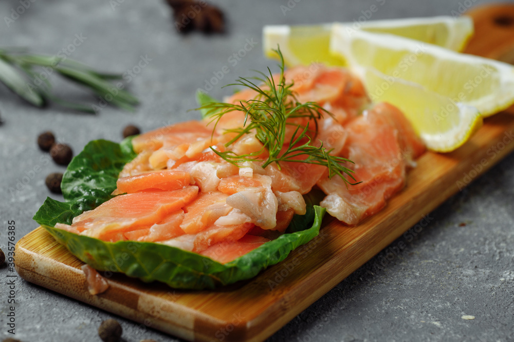 Pieces of fried salmon with dill and lemon wedges on a wooden board