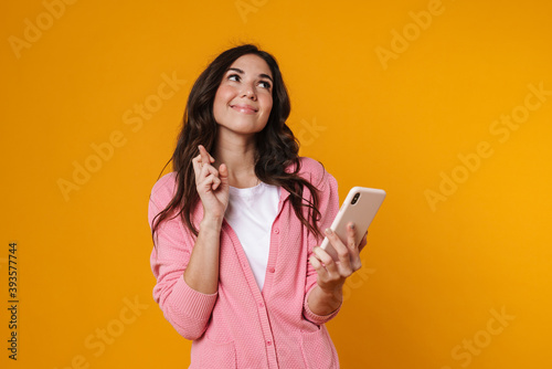 Joyful beautiful girl holding fingers crossed and using cellphone