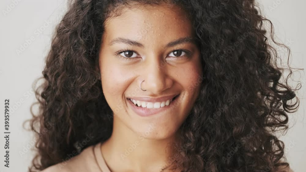 A close-up view of a smiling african american woman is winking to the camera standing isolated over beige background A close-up view of a smiling african american woman is winking to the camera standing isolated over beige background