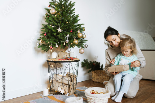 Mom and daughter decorate the Christmas tree in room.  Merry christmas and happy new year concept. Space for text. Family cozy moments. photo