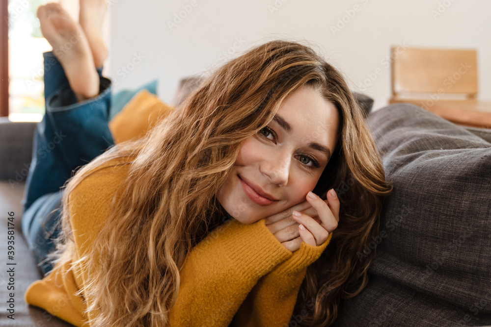 Fototapeta premium Joyful beautiful girl smiling at camera while lying on couch